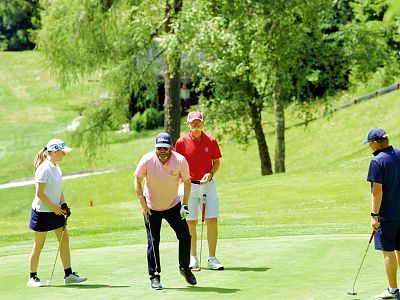 Four golfers enjoy a game on a green course surrounded by trees, under a clear sky on a sunny day.