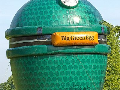 A large inflatable shaped like a green ceramic grill with 'Big Green Egg' logo, set outdoors against a clear sky and greenery.