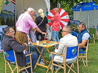 People gathered outdoors with a table and wheel, suggesting a fair or event setting.