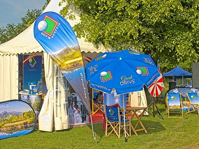 Outdoor booth with golf-themed designs, including banners, umbrellas, and a white tent on a sunny day.