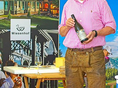 Man in Bavarian outfit holding a wine bottle amid a festive outdoor setting with Wiesenhof branding and joyful ambiance.
