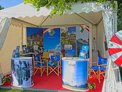 A booth with promotional banners, chairs, and brochures showcasing travel destinations, set on a red carpet under a canopy.