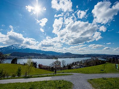 Scenic view of a bright sky with clouds over a lake and hills, with mountains in the distance under the sun.