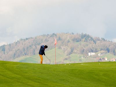 Person golfing on a lush green course with hills in background under a cloudy sky.