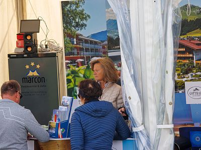 People at a travel booth with scenic posters and brochures promoting a vacation destination.