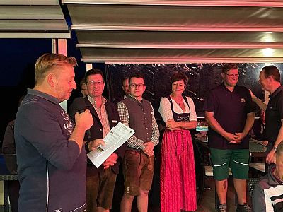 A group of five people in traditional Bavarian attire are gathered under a canopy. They seem to be engaged in conversation at an evening event.