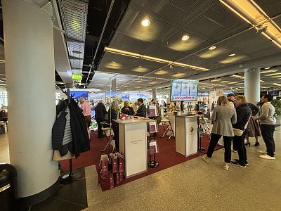 People browsing a duty-free shop at an airport, with various products and displays visible. The area is well-lit and bustling with activity.