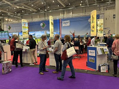 People engaging at a trade show, with colorful booths displaying various products and promotional materials in a large exhibition hall.