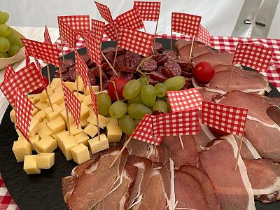 A platter with cold cuts, cheese, and grapes, decorated with red and white checkered flags, set on a checkered tablecloth.