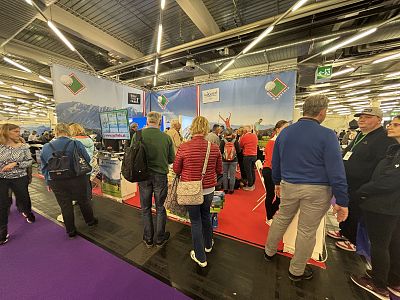 A busy trade show floor with attendees visiting booths, brightly lit with colorful displays. People are engaged in conversation and networking.