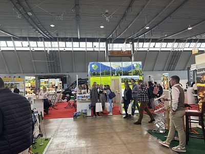 People walking and interacting at a trade show with various booths, lighting, and displays in a large exhibition hall.