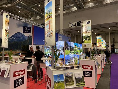Exhibition booth at a travel expo with colorful banners showcasing travel destinations. Visitors browse and interact with the displays highlighting scenic areas.