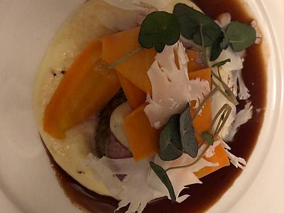 A gourmet dish with meat, sliced carrots, sauce, and green herbs on a white plate.