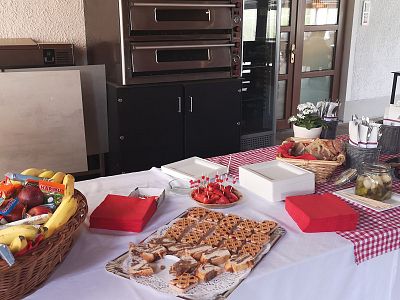 A buffet table with fruits, pastries, and snacks on a white tablecloth, surrounded by decorative items and cutlery, set indoors near a door.