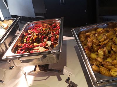 Buffet trays filled with colorful roasted vegetables and golden brown potatoes set on a table, ready to be served.