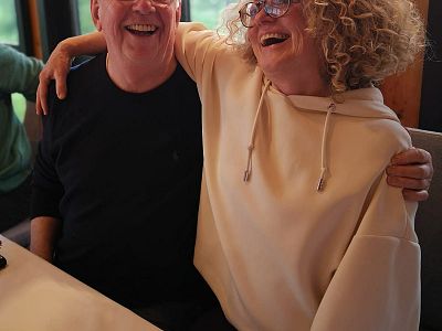 A man and woman sitting close, smiling and laughing. They appear to enjoy each other's company in a casual setting.