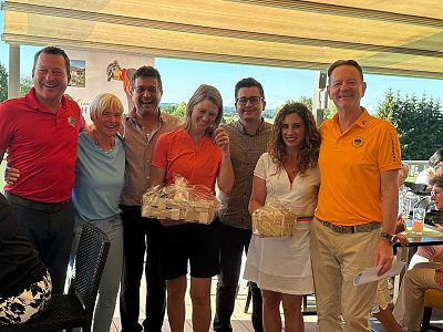 A group of seven smiling people under a canopy, holding gift baskets, suggesting a joyful gathering on a sunny day.