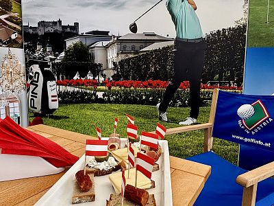 Display of Austrian snacks with flag toothpicks, a golfer's image in the background, and a golf-themed chair, depicting an Austrian-themed event.