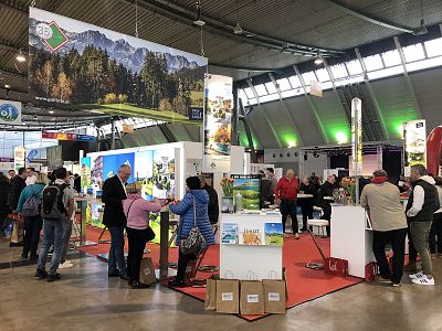 A trade show booth with people interacting, displaying colorful panels and promotional items under an industrial ceiling with bright lights.