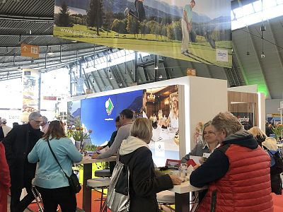 People interacting at a trade show booth with a scenic backdrop and promotional materials on display.