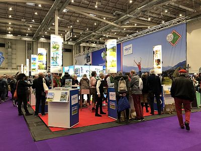 A busy trade show with attendees visiting various booths, high ceilings, and bright lighting in a large indoor venue.