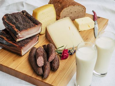 Wooden board with cheeses, sausages, bread, and two milk glasses on a white tablecloth.