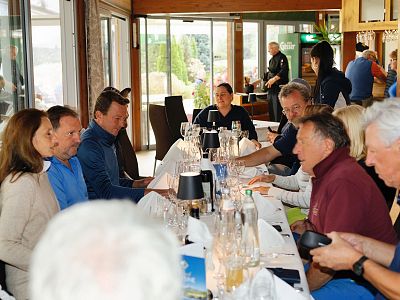 A group of people sit at a long table in a cozy restaurant, enjoying a meal and engaging in conversation. The setting is warm and inviting, with ambient lighting.