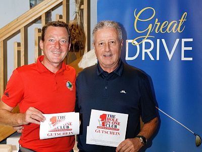 Two smiling men hold prize vouchers in front of a blue banner reading 'Great Drive,' possibly at a golf event or award ceremony.