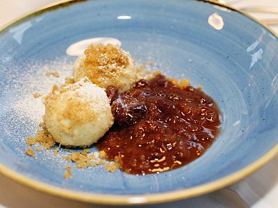 Two dumplings with sugar and breadcrumbs on a blue plate, next to a rich plum sauce, creating a sweet and inviting dessert presentation.