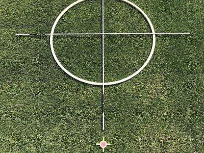 A circular target with crosshairs lies on a grassy field, used for alignment or sports activities.