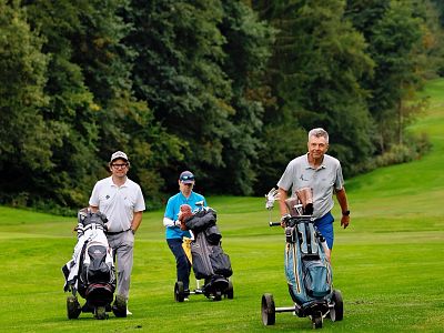 Three people on a golf course with golf carts, surrounded by greenery and trees, enjoying a day out in nature.