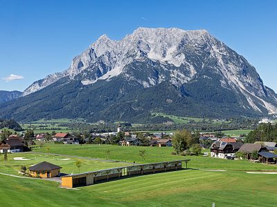 A landscape with a large mountain and a village with houses, green fields, and clear skies.