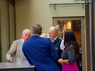 A group of people are engaged in conversation outside a building. Three men and one woman are standing near a counter, dressed in formal and casual attire.
