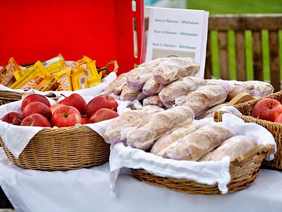 Baskets with red apples and wrapped sandwiches on a table with white cloth, against a red backdrop. Snacks and a wooden bench are partially visible.
