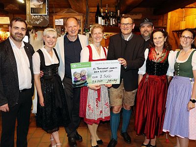 A group of people in traditional attire holding a large check in a rustic environment, suggesting celebration or festival.