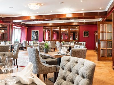 An elegantly furnished dining room with plush chairs, set tables, and warm lighting, creating a cozy and sophisticated atmosphere.