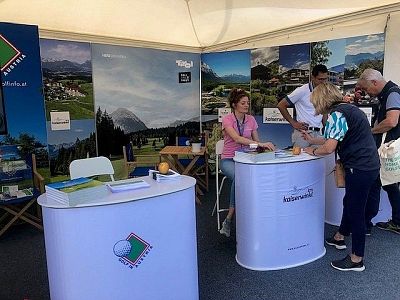 A booth with colorful images of landscapes and people interacting with staff, highlighting a travel destination at an event.