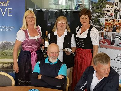 Group of people, some in Bavarian attire, pose smiling indoors with promotional posters in the background.