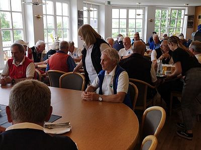 A group of older adults seated inside a café, chatting and enjoying drinks. The room is bright with natural light from large windows, creating a cheerful ambiance.