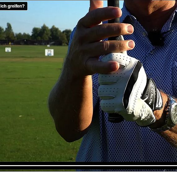 A golfer demonstrates the proper grip on a golf club with hands wearing a glove, set against a green golf course backdrop under a clear sky.