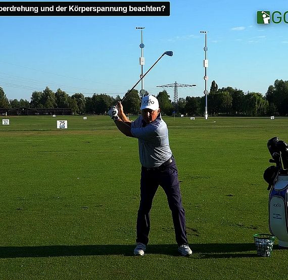 Golfer demonstrating swing on green course with golf bag, under clear skies, trees in background. Practicing posture and technique.