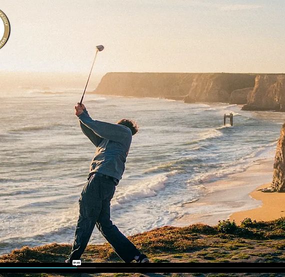 A golfer swings by a cliff overlooking the ocean with waves crashing below, under a golden sunset sky.