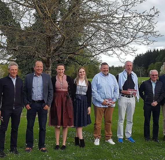 Ten people standing on grass with trees and cloudy sky in the background, dressed in smart-casual clothing, posing for a group photo.