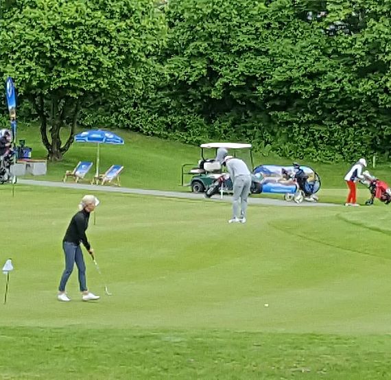 People on a green golf course practicing putting, surrounded by trees and golf carts. A peaceful scene with a focus on the sport.