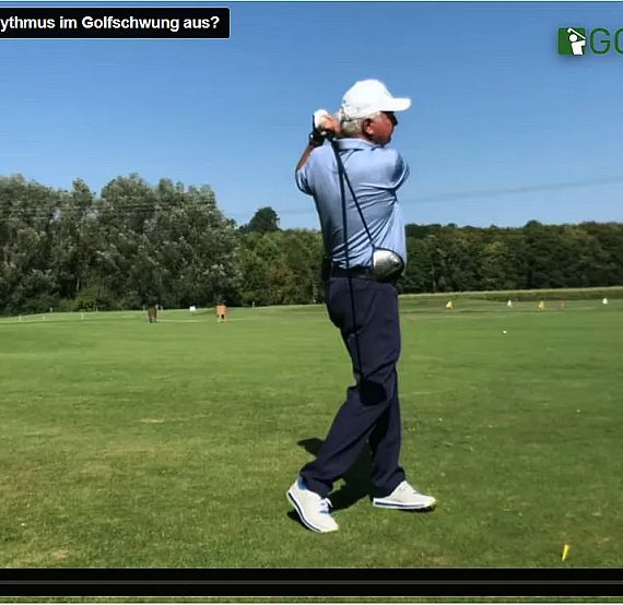 A golfer in mid-swing on a lush green course under a clear sky.