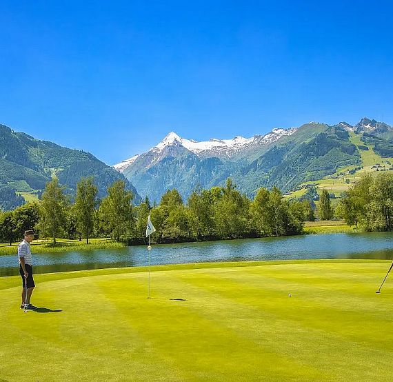 Two golfers on a green golf course surrounded by mountains and a lake.