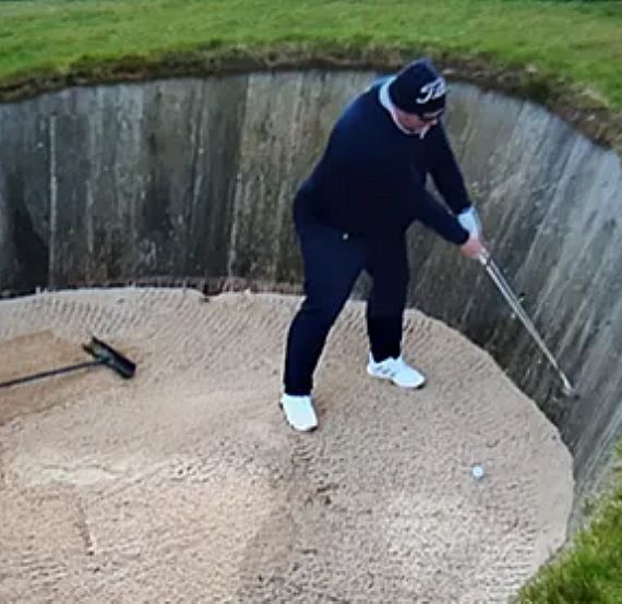 A golfer in a deep sand bunker with high wooden walls is preparing to hit a shot, showcasing a challenging position on the course.