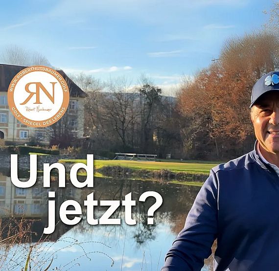 A man stands by a lake with trees and a building in the background. He's wearing a cap and smiling. Text reads 'Und jetzt?'
