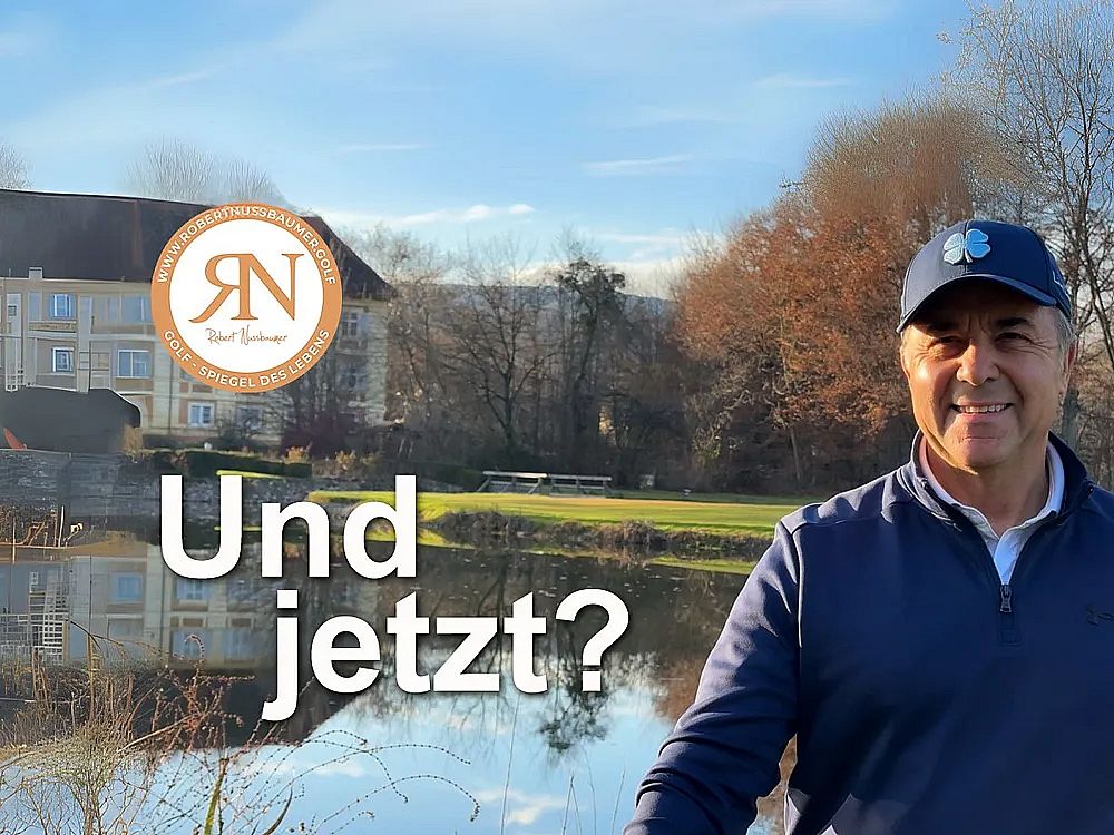 A man stands by a lake with trees and a building in the background. He's wearing a cap and smiling. Text reads 'Und jetzt?'