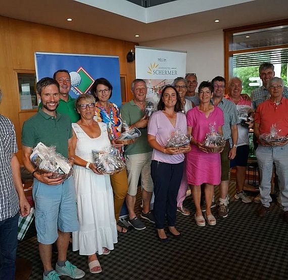 A group of people inside, smiling and holding gift baskets, indicating a celebration or gathering, with banners in the background.